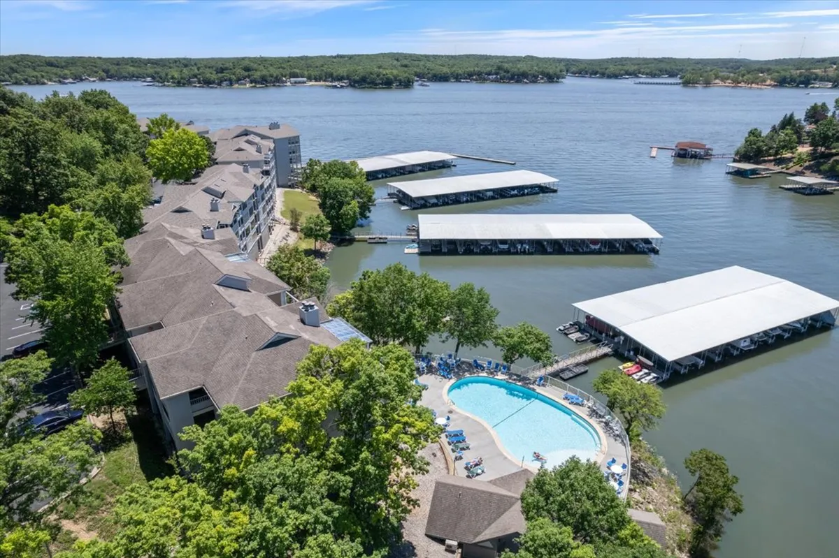This image captures a vibrant outdoor pool surrounded by lush greenery, with a marina featuring boat docks visible just beyond the pool area. Guests are seen swimming and sunbathing, while the tranquil waterfront setting suggests opportunities for boating and social gatherings.