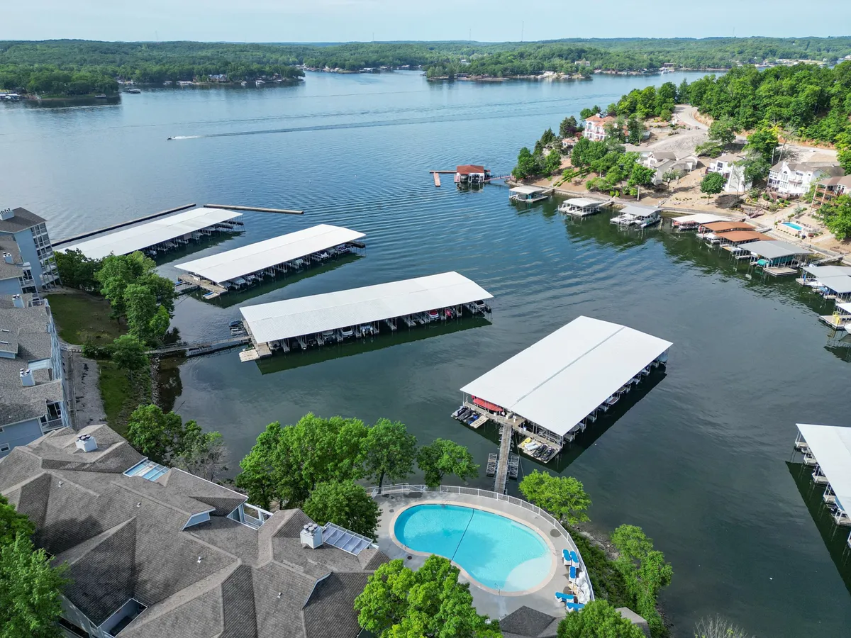 A serene exterior perspective showing both the swimming pool and boat docks nestled beside calm water, framed by abundant greenery. The tranquil setting invites relaxation and showcases areas for swimming, boating, and gathering by the water's edge.