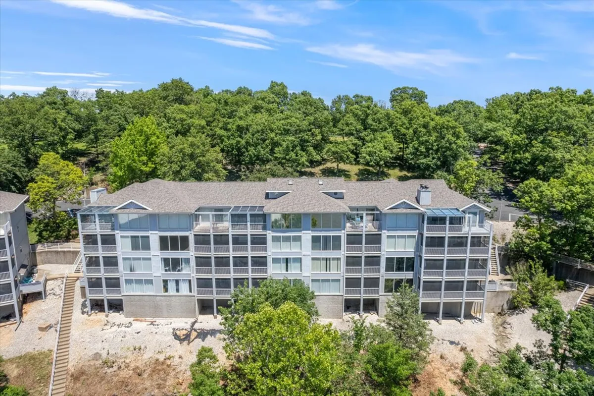 A wide view of the building’s modern exterior with green landscaped grounds and a stairway leading to the entrance. The image also captures the peacefulness of the surroundings, with nearby green spaces and subtle hints of water views, inviting residents to explore walking trails or enjoy the outdoors.