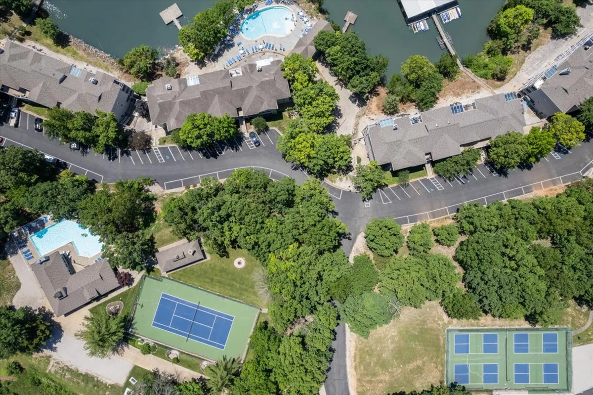 A wide view of the community grounds reveals two sparkling swimming pools, tennis/pickleball courts, lush landscaping, and waterfront access. The vibrant, active scene is ideal for showcasing group amenities and recreational opportunities.