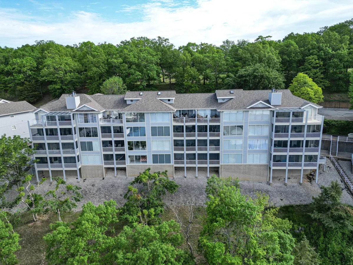 A multi-story building surrounded by mature trees with several balconies visible. The building is set in a tranquil, green setting, showcasing the inviting outdoor spaces perfect for relaxing or taking a break from work. The balconies are ideal spots for enjoying lake views or fresh air during remote work sessions.