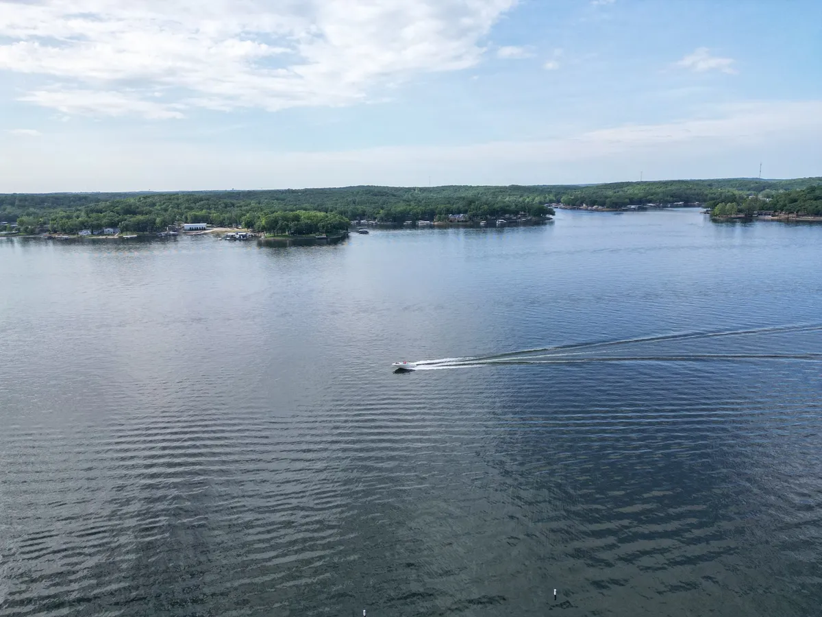 A calm lake surface stretches out under an open sky, with a boat gliding across the water and lush green hills in the background. The scene is peaceful and inviting, emphasizing the enjoyment of boating and scenic relaxation on the lake.