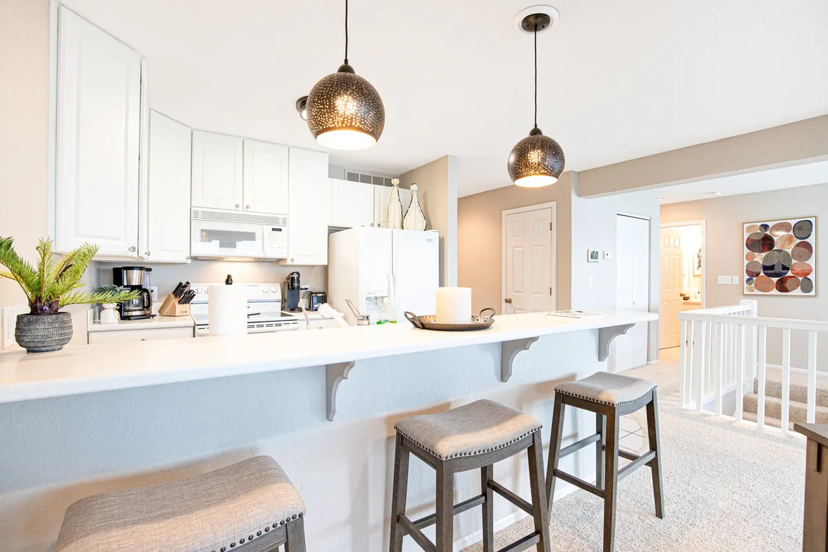 A beautifully renovated kitchen with a central island, bar stools for casual seating, stylish hanging light fixtures above, and a decorative bowl as a centerpiece. The modern layout and inviting colors make this kitchen feel both functional and social.