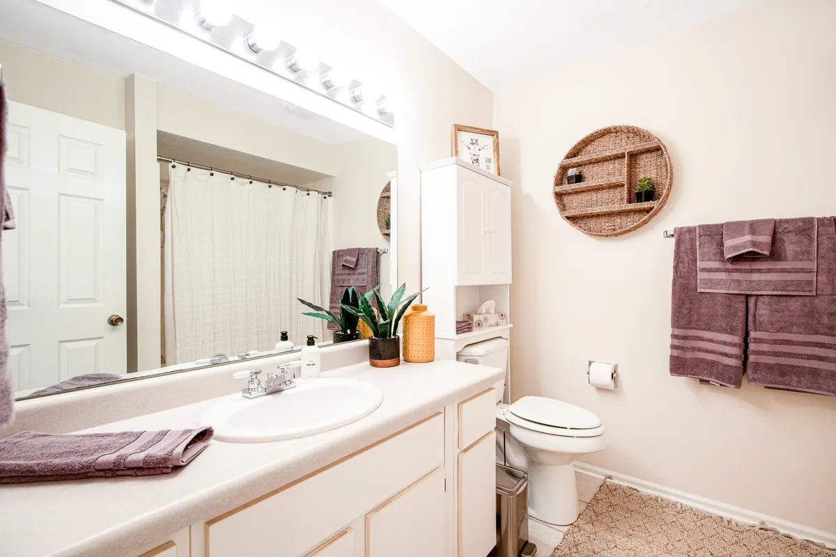 A modern bathroom with a sleek vanity, mirror, fresh towels, decorative shelves, and a touch of greenery. The space is well-organized and bathed in calming, natural light—ideal for personal care routines and a soothing start or end to the day.