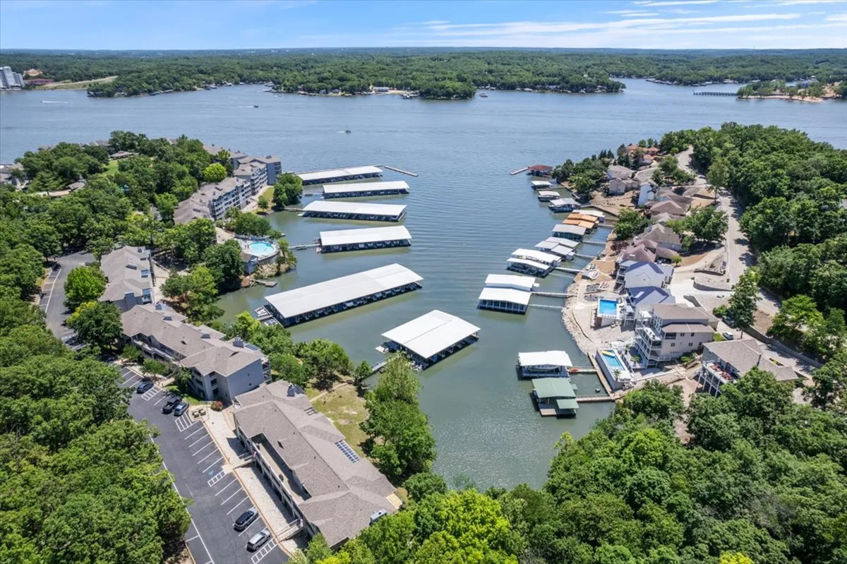 An aerial view showcases the lake, marinas, residential buildings, a pool area, and abundant greenery. The image conveys both the recreational amenities and the picturesque environment, giving a broader sense of the setting and nearby activities.